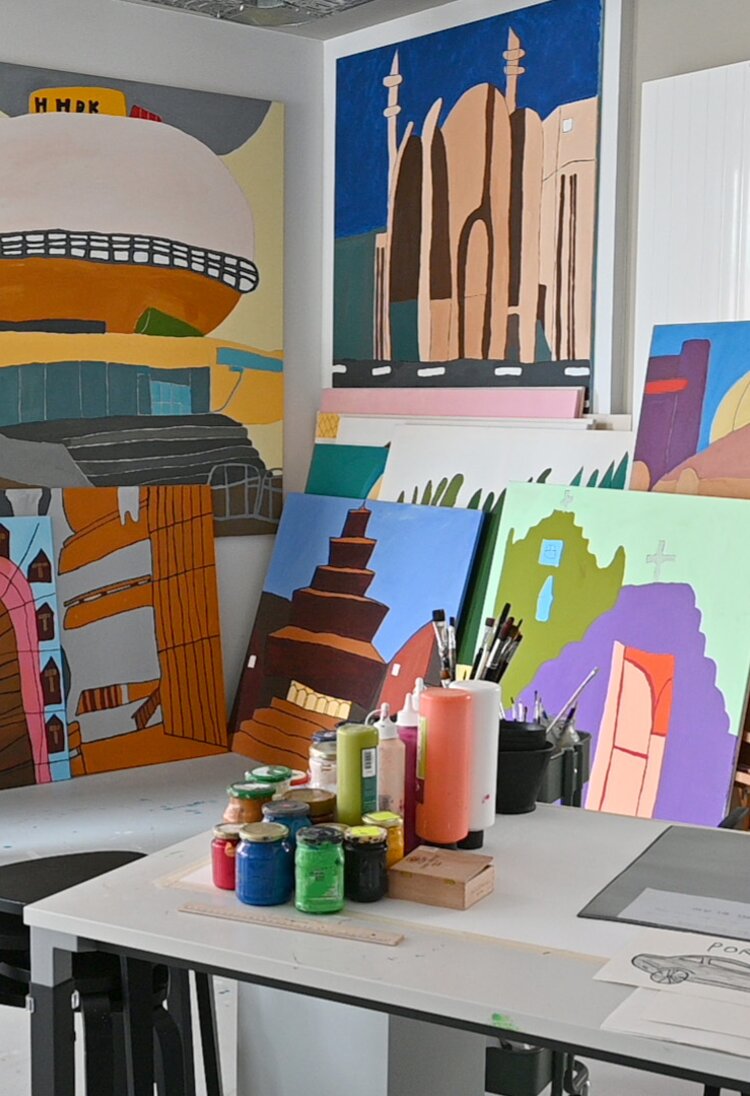 Im Vordergrund steht ein großer Tisch mit Pinseln, Farben und Zeichnungen. Im Hintergrund lehnen an der Wand Leinwände mit fertigen Werken. | © kaethe:k Kunsthaus
