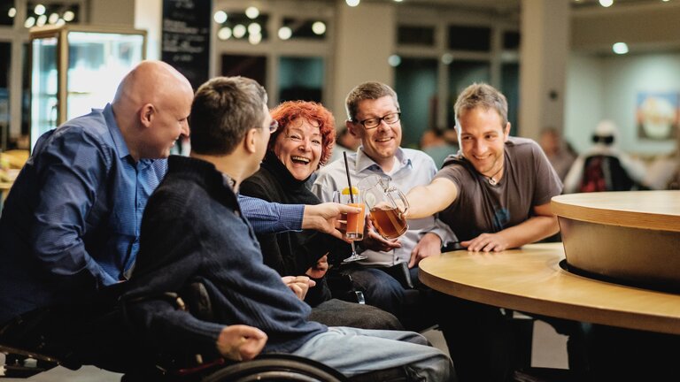 Menschen mit Behinderungen in Interaktion mit ihren Assistenzen in einer Bar. | © Andi Weiland/Gesellschaftsbilder.de