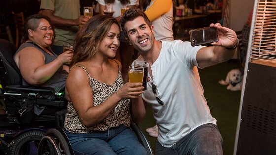 eine Frau im Rollstuhl und ein Mann machen ein Selfie mit Getränken in der Hand | © ELEVATE / pexels.com