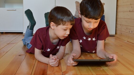 Es liegen zwei Jungen mit rotem Tshirt auf dem Boden. Der Junge auf der rechten Seite hat ein Tablet in der Hand. Beide schauen rein. | © Viki_B / pixabay.com