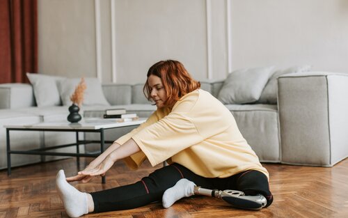 Eine Frau mit einem amputierten Bein sitzt auf dem Boden und dehnt sich | © Vlada / pexels.com