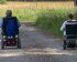  zwei Personen fahren nebeneinander auf einem Schotterweg mit einem elektrischen Rollstuhl. Das Bild ist von hinten aufgenommen, es ist ein schöner Tag. | © pixabay.com