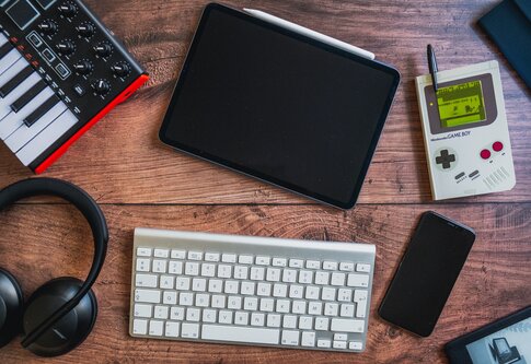 Auf einem Tisch liegt ein Handy, eine Tastatur, ein Tablet, ein Game Boy und Kopfhörer | © Audric Wonkam / Unsplash