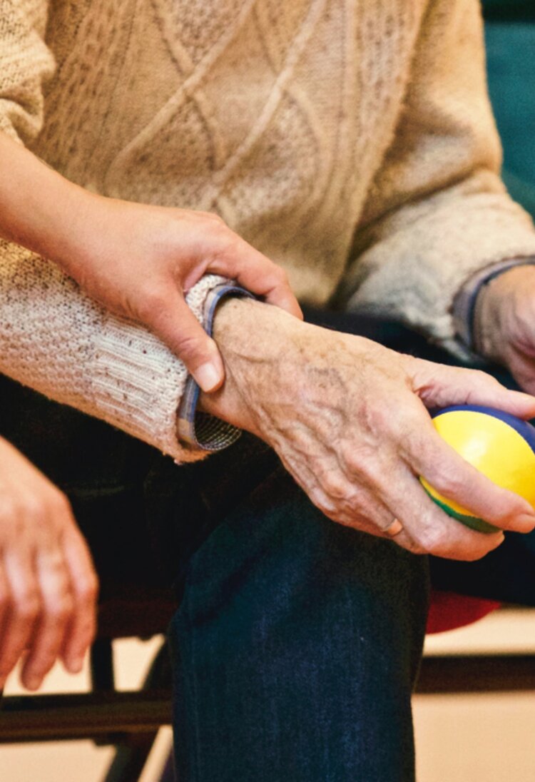 Man sieht die Hände eines älteren Mannes, die einen bunten Softball halten. Ein weibliche Hand liegt auf seinem Arm. | © Matthias Zomer / Pexels.com 