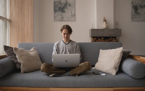 Ein junger Mann sitzt in seinem Wohnzimmer auf der Couch und arbeitet am Laptop | © Ekaterina Bolovtsova / pexels
