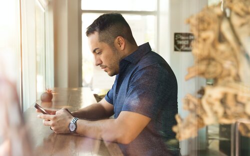 Ein Mann an einem Stehtisch in einem Café sieht auf sein Smartphone. | © unsplash