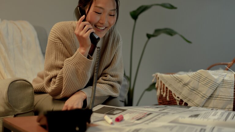Eine Frau sitzt mit dem Telefonhörer am Ohr vor einer Zeitung | © pexels