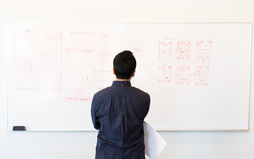 Ein Mann steht vor einem Whiteboard mit technischen Skizzen und schaut es sich an | © Christina Morillo / pexels