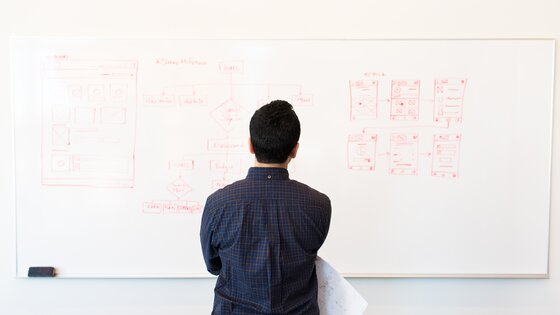 Ein Mann steht vor einem Whiteboard mit technischen Skizzen und schaut es sich an | © Christina Morillo / pexels