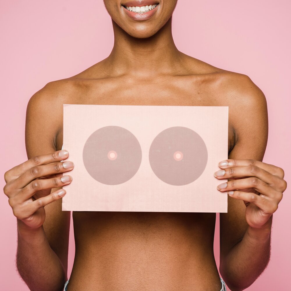 Eine Frau hält ein Schild mit Brüsten vor ihre Brüste | © Klaus Nielsen / pexels