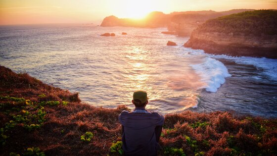 Ein Mann sitzt an einer Klippe und betrachtet den Sonnenuntergang | © Haydan Assoendawy / pexels