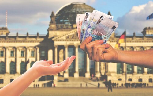 Das Bild zeigt zwei Hände vor einem Regierungsgebäude. Die eine Hand reicht der anderen Hand Geldscheine: Drei 20€ Scheine und einen 10€ Schein. | © Pixabay
