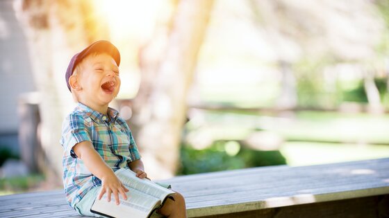 Ein kleiner Junge sitzt auf der Bank und lacht fröhlich | © unsplash