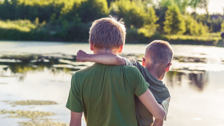 Zwei jüngere Brüder halten sich am See in den Armen | © Vitolda Klein / unsplash