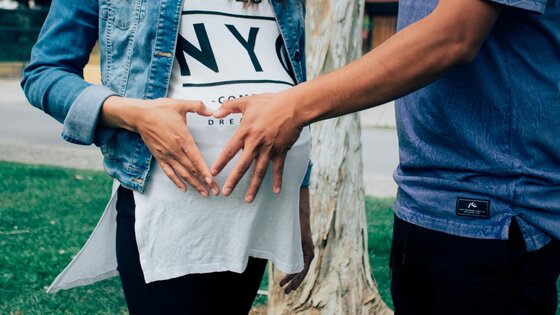 Ein Pärchen bildet mit den Händen ein Herz vor dem Bauch der Schwangeren | © pexels