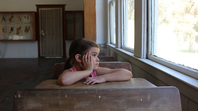 Ein Mädchen sitzt an einem Schulpult und sieht aus dem Fenster | © pixabay