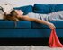 Eine junge Frau liegt auf einem blauen Sofa. Einen Arm hält sie dabei über den Kopf, der andere Arm hängt leicht über das Sofa hinaus und hält ein rotes Tuch in der Hand.  | © Pexels