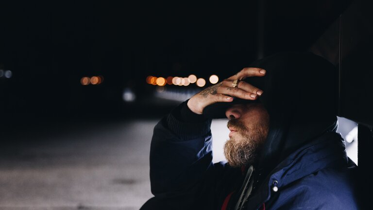 Mann sitzt im Dunkeln draußen und hält eine Hand an die Schläfe. | © Jonathan Rados/ unsplash