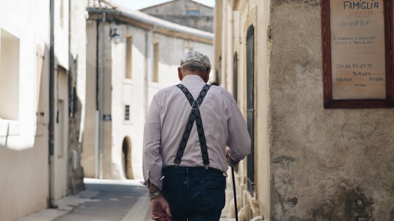 Foto von einem älteren Herren, der mit einem Stock durch eine Gasse läuft. | © Unsplash