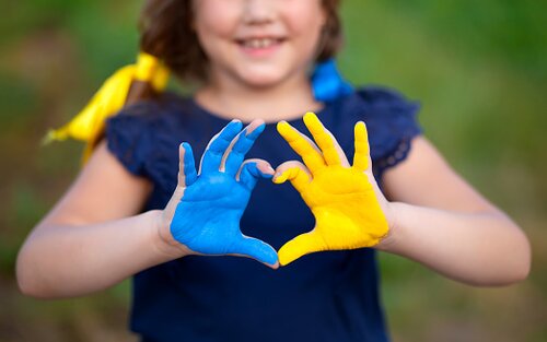 Ein Kind zeigt ein Herz mit den Händen. Die Hände wurden in den Farben der Ukraine (Blau, Gelb) bemalt.