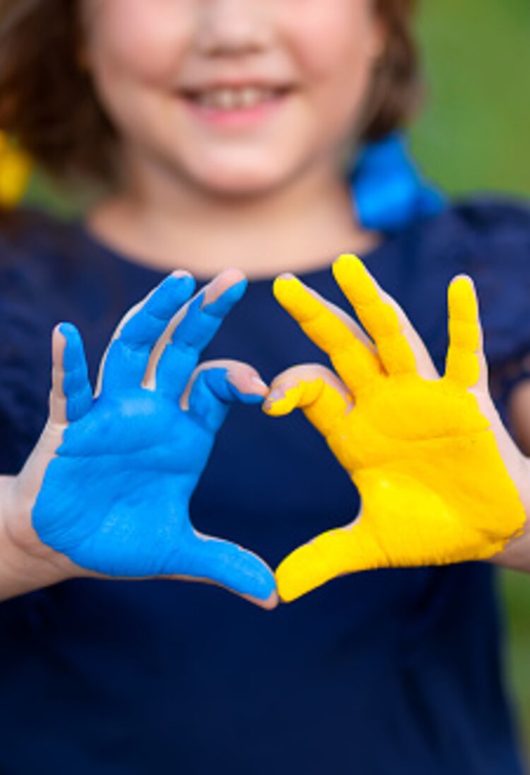 Ein Kind zeigt ein Herz mit den Händen. Die Hände wurden in den Farben der Ukraine (Blau, Gelb) bemalt.