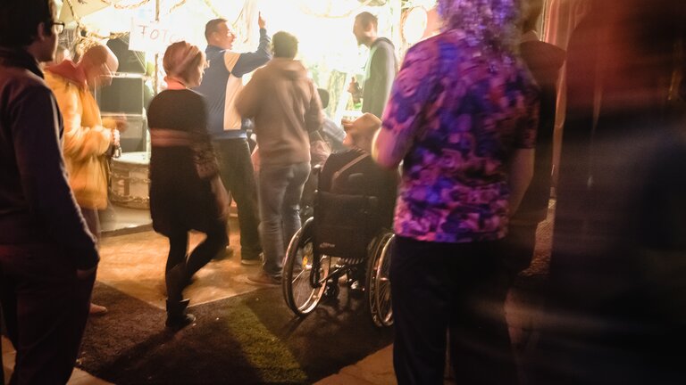 Bild mit Menschen und unteranderem einem Rollstuhlfahrer vor einem Eingang einer Party | © Andi Weiland / Gesellschaftsbilder.de