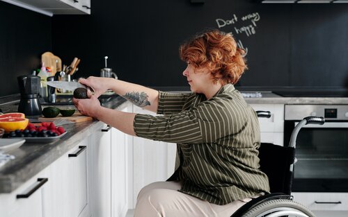 eine Frau sitzt im Rollstuhl vor einer Küchenzeile und schneidet eine Avocado | © Pexels Marcus Aurelius