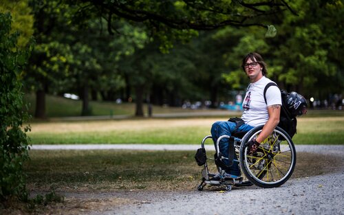 Ein Mann, der im Rollstuhl sitzt, in einem Park mit vielen Bäumen | © Jörg Farys | Gesellschaftsbilder.de