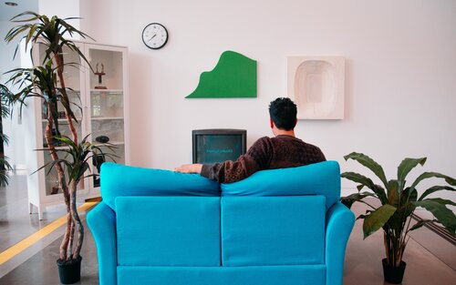 Mann sitzt auf einem blauen Sofa und sieht Fernseh. | © unsplash