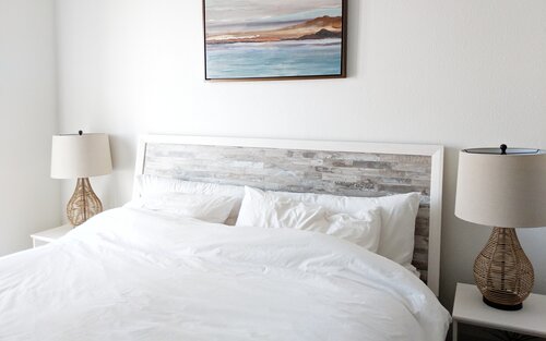 Ein Doppelbett mit einer weißen Decke und Kissen. Auf beiden Seiten befindet sich ein Nachttisch mit einer Lampe. Über dem Bett hängt ein Gemälde mit einer Landschaft.  | © Nienke Witteveen Fleuren/unsplash