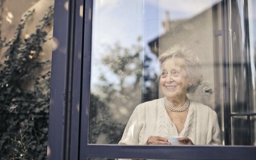 Eine ältere Frau guckt aus einem Fenster und lächelt. | © pexels