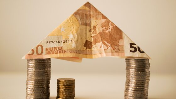kleines Haus, dessen Wände aus einem Stapel Geldmünzen besteht und ein Dach aus einem gefalteten 50 Euro Schein hat | © pexels