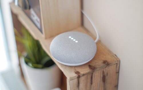 Kleiner runder Lautsprecher mit intelligenter Technologie auf einem Holzregal | © pexels