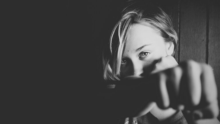 Schwarz-Weiß Foto von einer Frau, die in die Kamera schaut und die geballte Faust ausstreckt. | © Unsplash