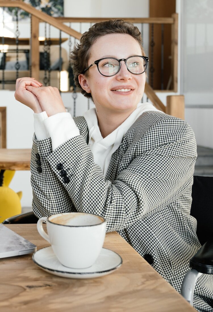 Eine Frau im Rollstuhl sitzt im Café und blickt lächelnd in die Ferne. | ©  SHVETS production / pexels.com