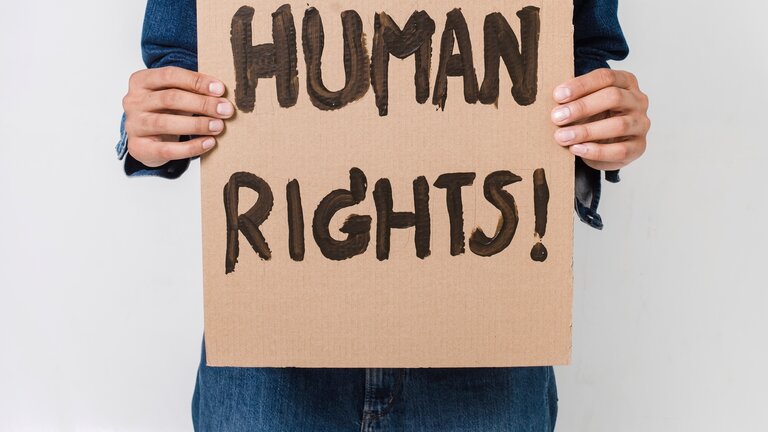 Man sieht zwei Hände, die ein Pappschild halten, auf das mit schwarzer Farbe „Human Rights“ geschrieben wurde. | © Sora Shimazaki / Pexels.com
