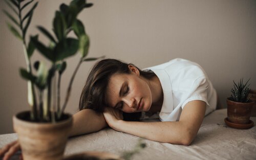 Eine junge Frau sitzt an einem Tisch und hat ihren Kopf auf ihren rechten Arm gelegt, der ausgetreckt auf einem Tisch anliegt. Ihre Augen sind geschlossen und sie schläft.  | © Pexels Valeria Ushakova