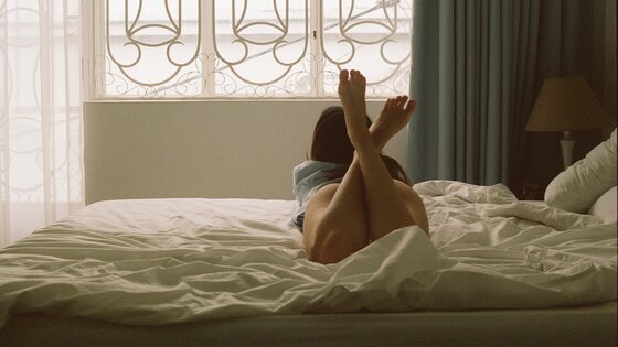 Eine Frau liegt auf dem Bauch im Bett und schaut aus dem Fenster | © Dương Nhân / pexels