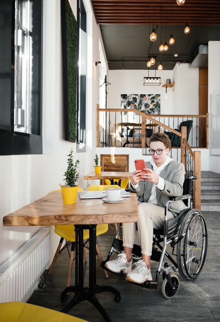 Frau im Rollstuhl sitzt in Café und schaut auf ihr Smartphone. | © Pexels /Shvets Production