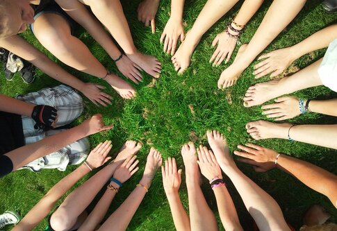 Eine Gruppe von Menschen sitzt im Kreis zusammen. Sie halten alle ihre Hände und Füße nach vorne in den Kreis hinein. Foto ist aus der Vogelperspektive aufgenommen. | © pexels