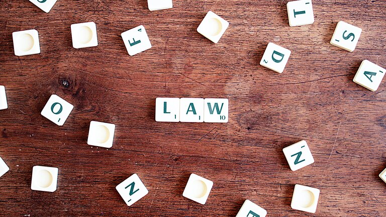 Auf einem Holztisch liegen mehrere Scrabble-Buchstaben. Drei von ihnen sind zum Wort Law angeordnet. | © Pexels.com