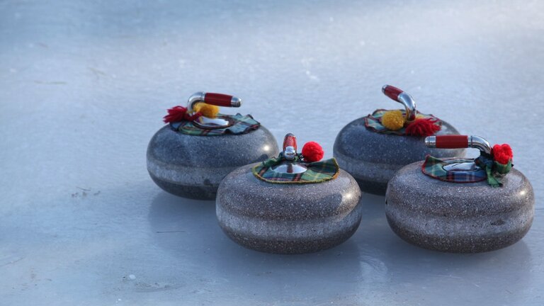 Vier Curlingsteine auf Eis. An den Griffen der Curlingsteine befinden sich gelbe und rote Bommel. | © Amber McNulty/ pixabay