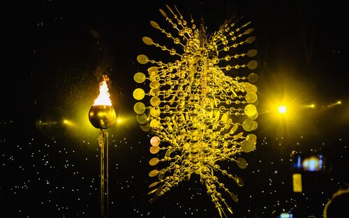 Neben einer erleuchteten Fackel ist eine schwebende Skulptur, die aus goldenen Blasen besteht, zu sehen. | © Andi Weiland/ Gesellschaftsbilder.de