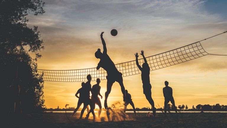 Foto von einer Gruppe Menschen, die im Sonnenuntergane Volleyball spielen. | © Unsplash