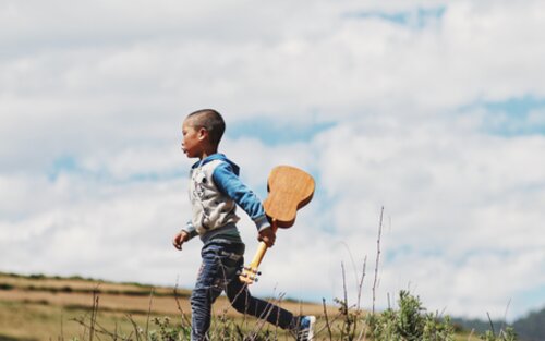 Ein Junge rennt mit einer Ukulele in der Hand über ein Feld | © unsplash