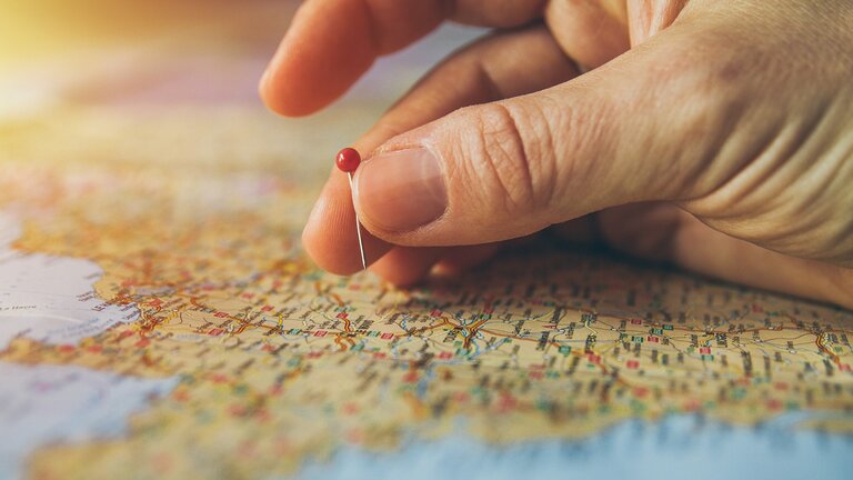 Nahaufnahme einer Hand, die eine Stecknadel in eine Weltkarte steckt | © Pixabay