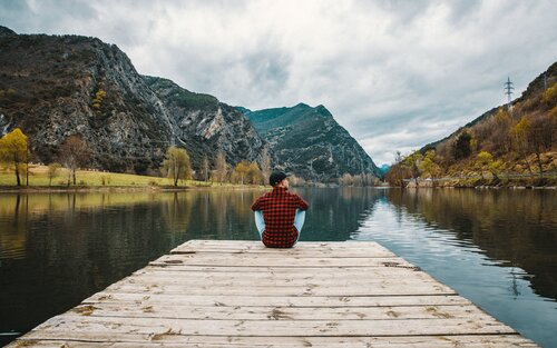 Eine Person sitzt auf einem Steg am See, mit den Bergen im Hintergrund | © Jannes Jacobs/unsplash