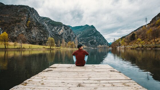 Eine Person sitzt auf einem Steg am See, mit den Bergen im Hintergrund | © Jannes Jacobs/unsplash