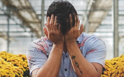 Bild eines Mannes, der inmitten von Blumen sitzt und den Kopf in die Hände gestützt hat. Er weint offensichtlich. | © pexels